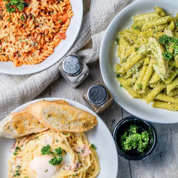 Three plates of pasta and garlic bread on a wooden table