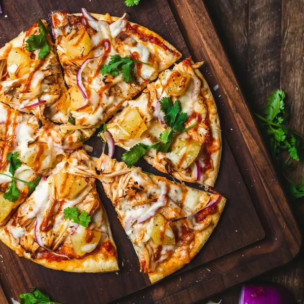 A sliced pizza with chicken, pineapple and red onion on a wooden board