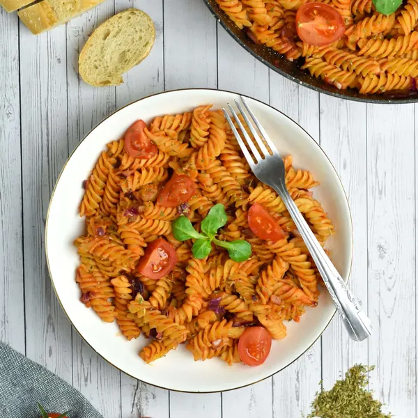 A plate of fusilli with cherry tomatoes and basil beside sliced bread